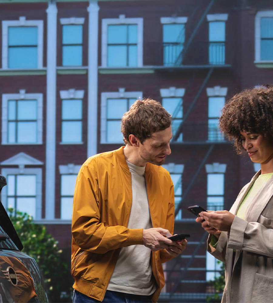 Man and woman looking at phone next to parked MINI